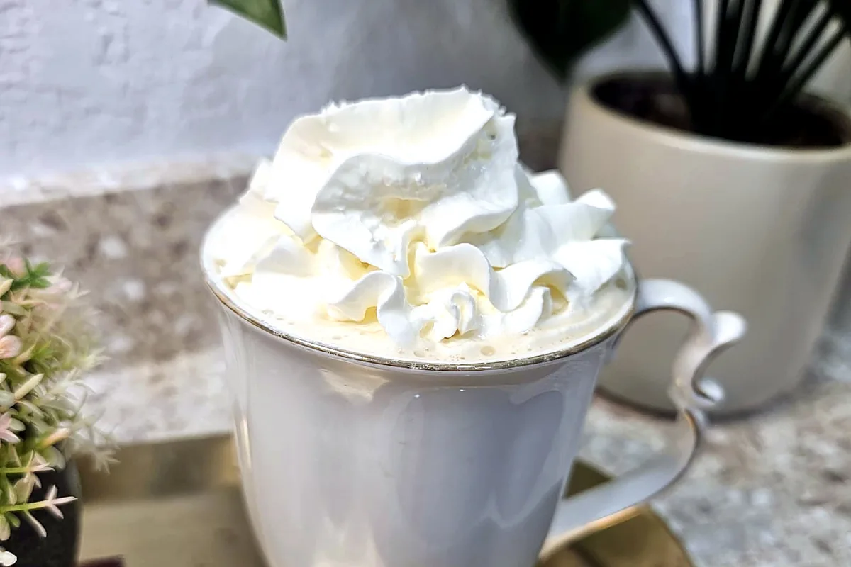 A hot espresso with whipped cream in a gold-rimmed cup, on a brass tray next to flowers